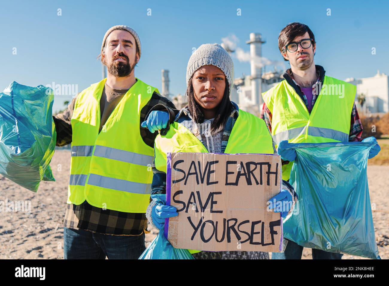 Squadra di attivisti o volontari, raccogliendo rifiuti dalla spiaggia, tenendo un poster che dice salvare la terra salvarsi. Un gruppo di giovani pulisce la spazzatura della sabbia. Foto di alta qualità Foto Stock
