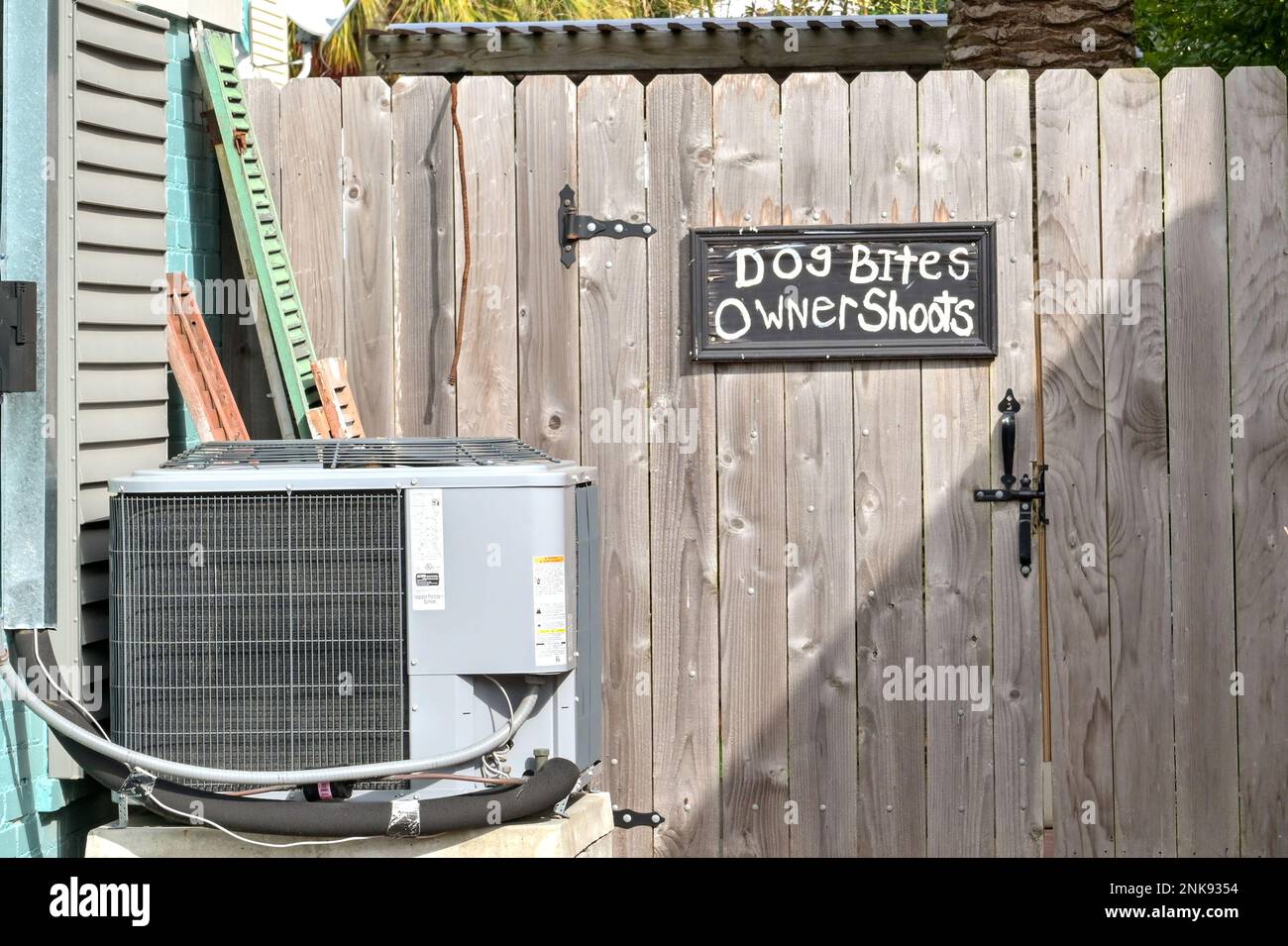 Galveston, Texas - 2023 febbraio: Umorismo sul segno su recinto di una proprietà residenziale che avverte che il cane morde e il proprietario spara una pistola Foto Stock