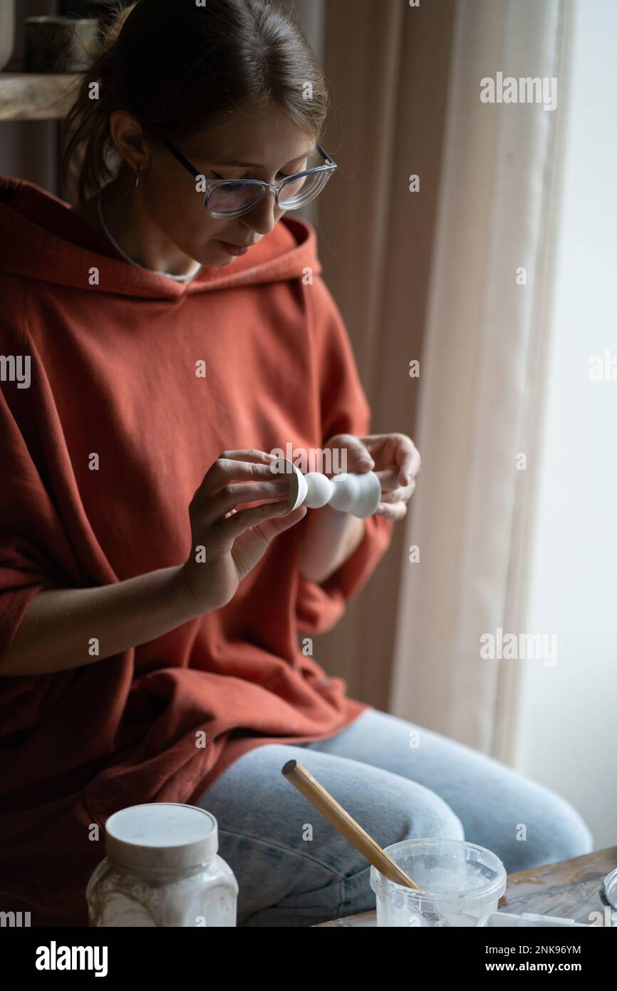 Scultore donna concentrato che fa figurine in porcellana in miniatura ricoperte di vernice bianca Foto Stock