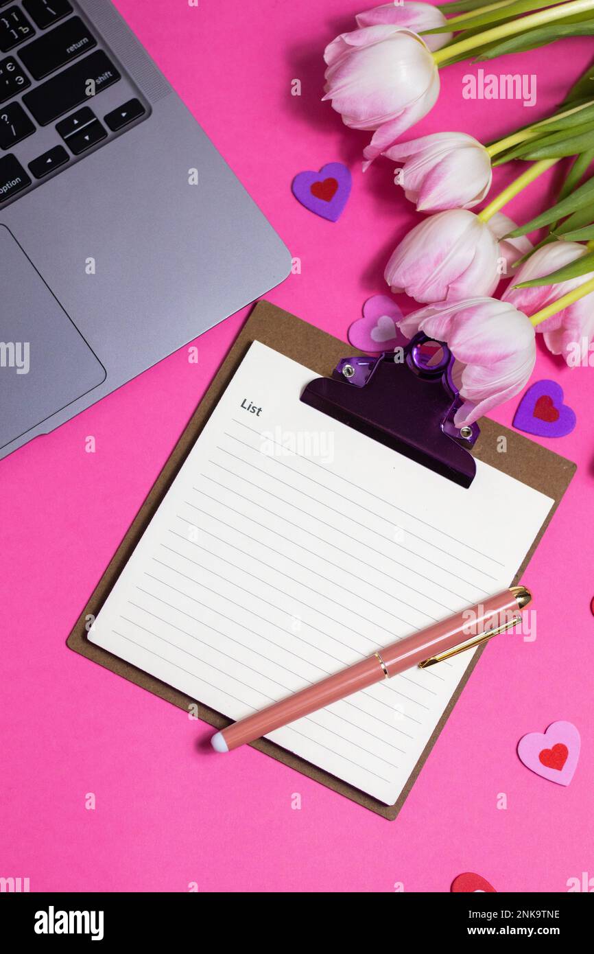 Scrivania da ufficio per donne con fiori e vista dall'alto. Spazio di lavoro femminile con computer portatile, tulipani, accessori, notebook, tazza di caffè su sfondo rosa. Hol Foto Stock