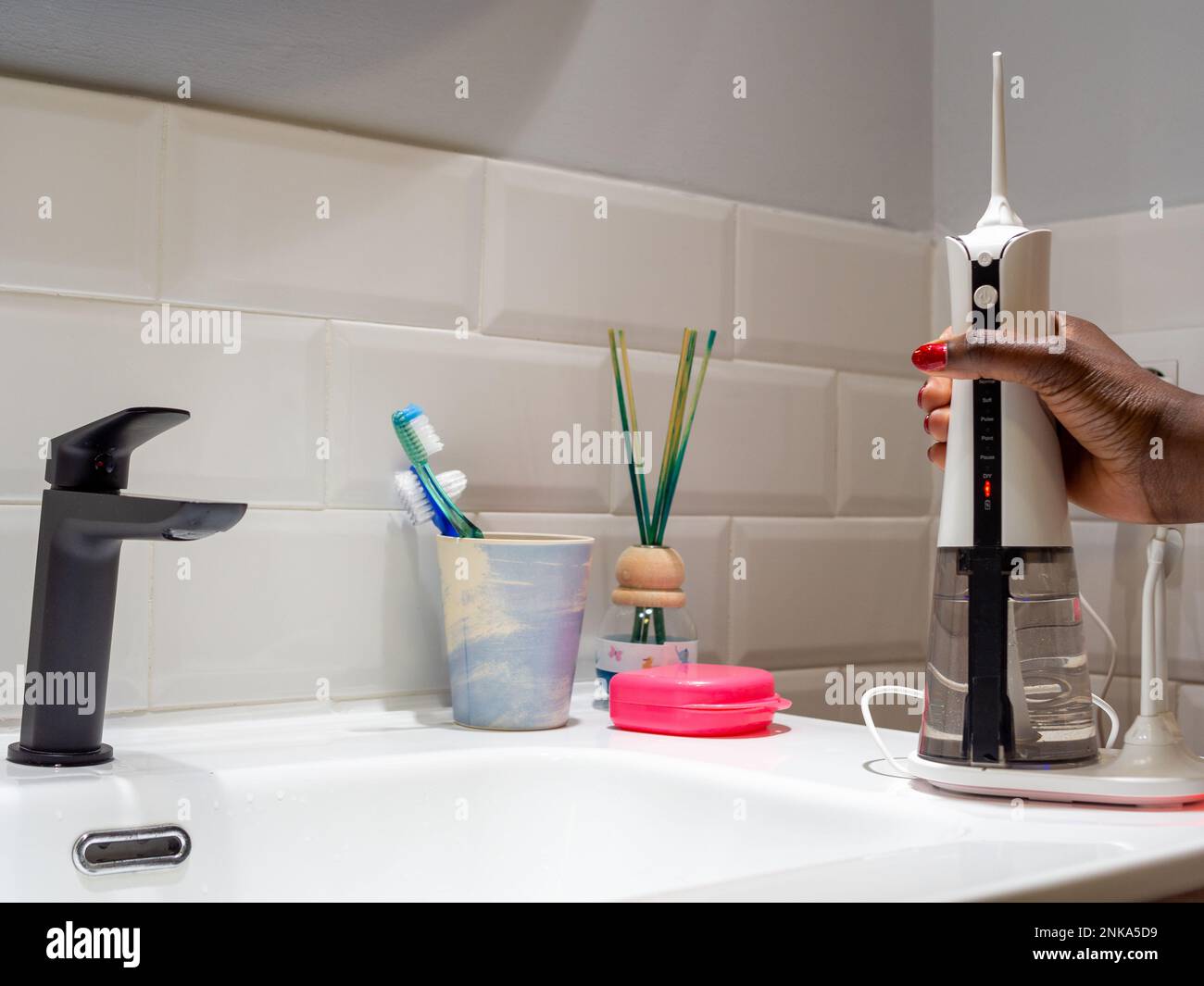 giovane donna che tiene un wirelcome flosser d'acqua domestico sul lavabo del bagno Foto Stock