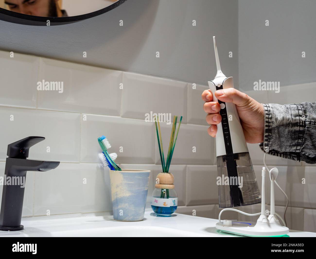 un giovane uomo che tiene un galleggiante per acqua dentale domestica wireless sul lavabo del bagno Foto Stock
