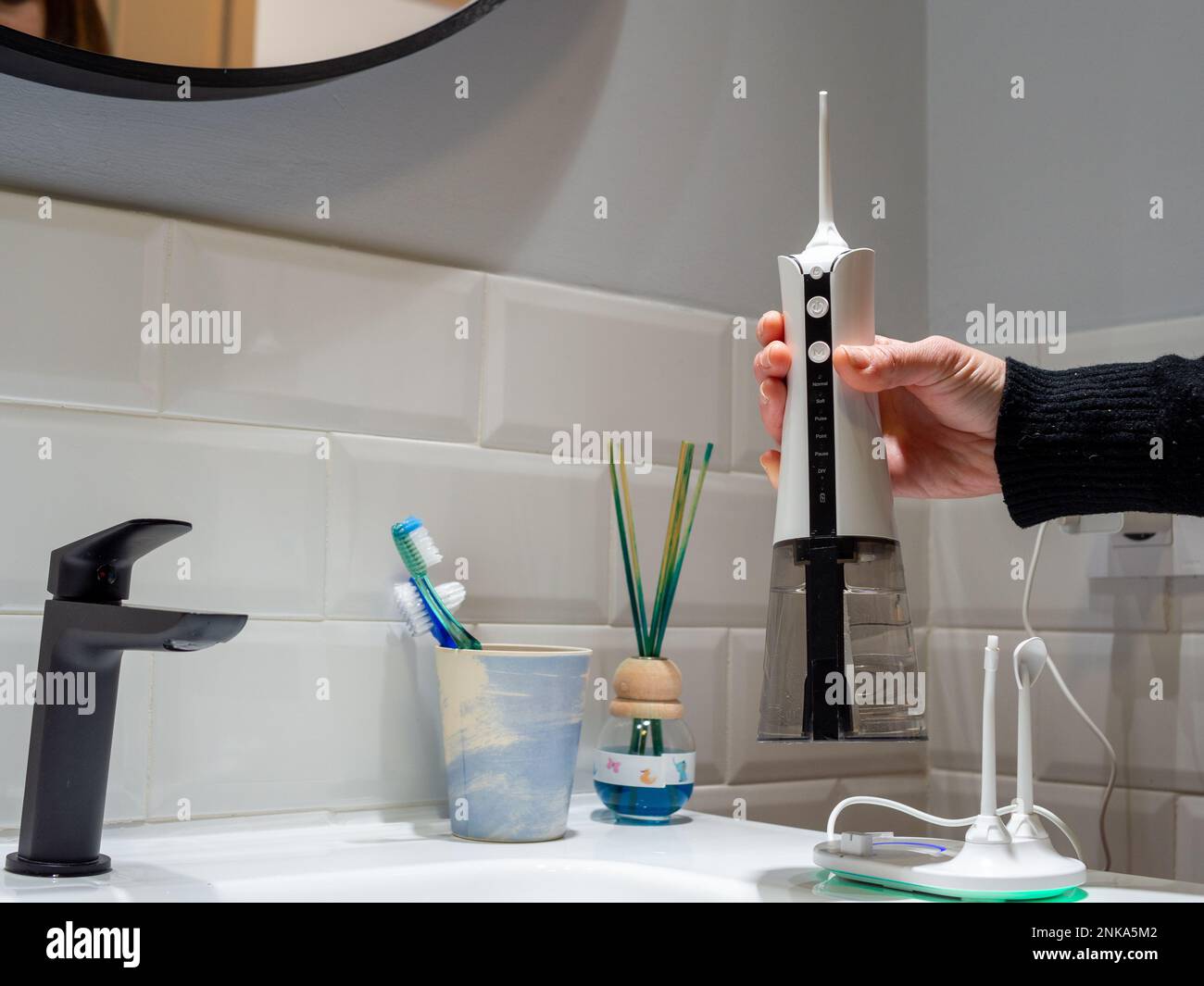 giovane donna che tiene un wirelcome flosser d'acqua domestico sul lavabo del bagno Foto Stock