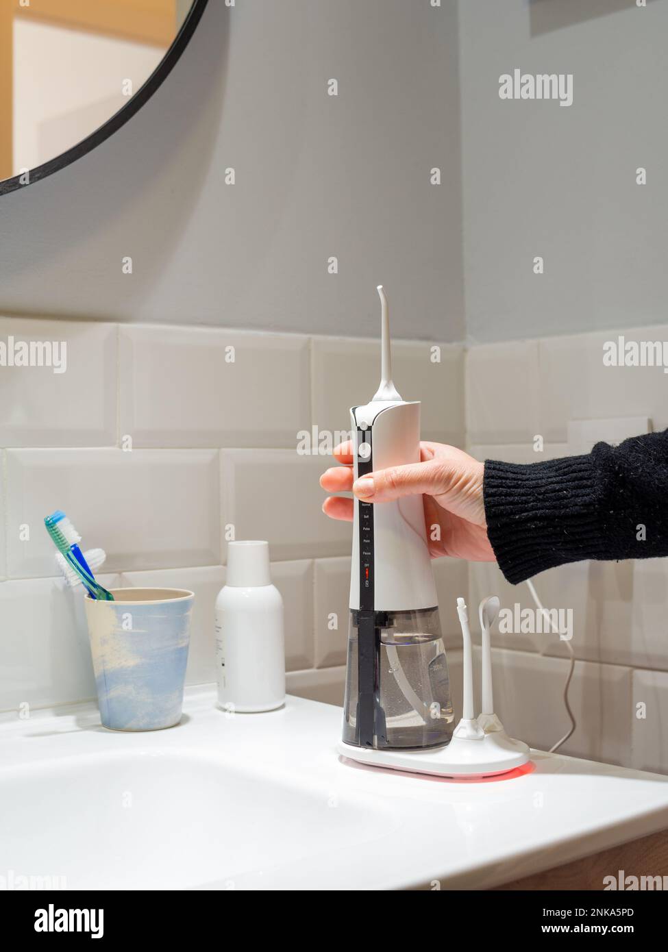 giovane donna che tiene un wirelcome flosser d'acqua domestico sul lavabo del bagno Foto Stock
