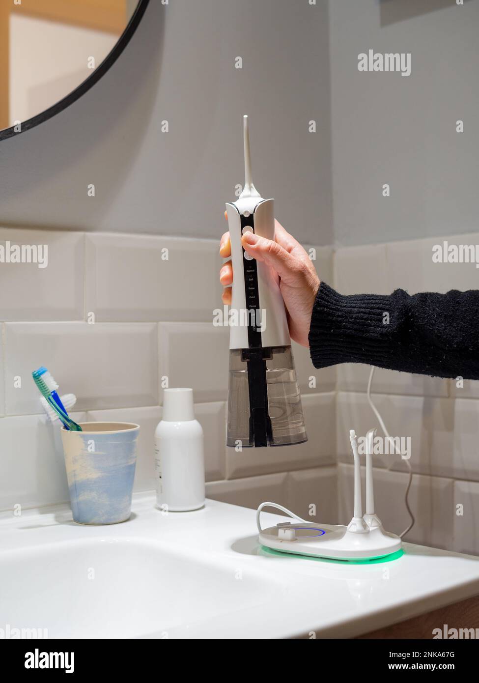 giovane donna che tiene un wirelcome flosser d'acqua domestico sul lavabo del bagno Foto Stock