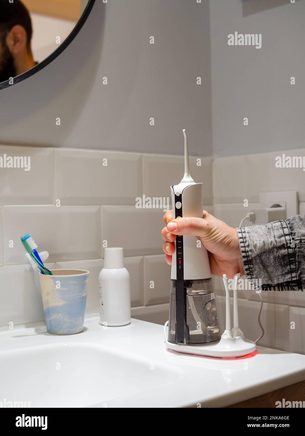 un giovane uomo che tiene un galleggiante per acqua dentale domestica wireless sul lavabo del bagno Foto Stock