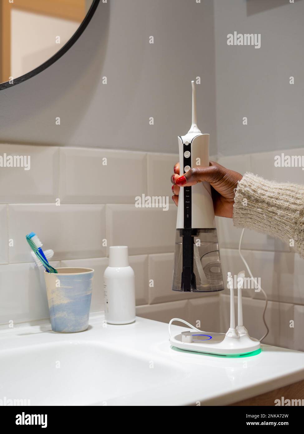 giovane donna che tiene un wirelcome flosser d'acqua domestico sul lavabo del bagno Foto Stock