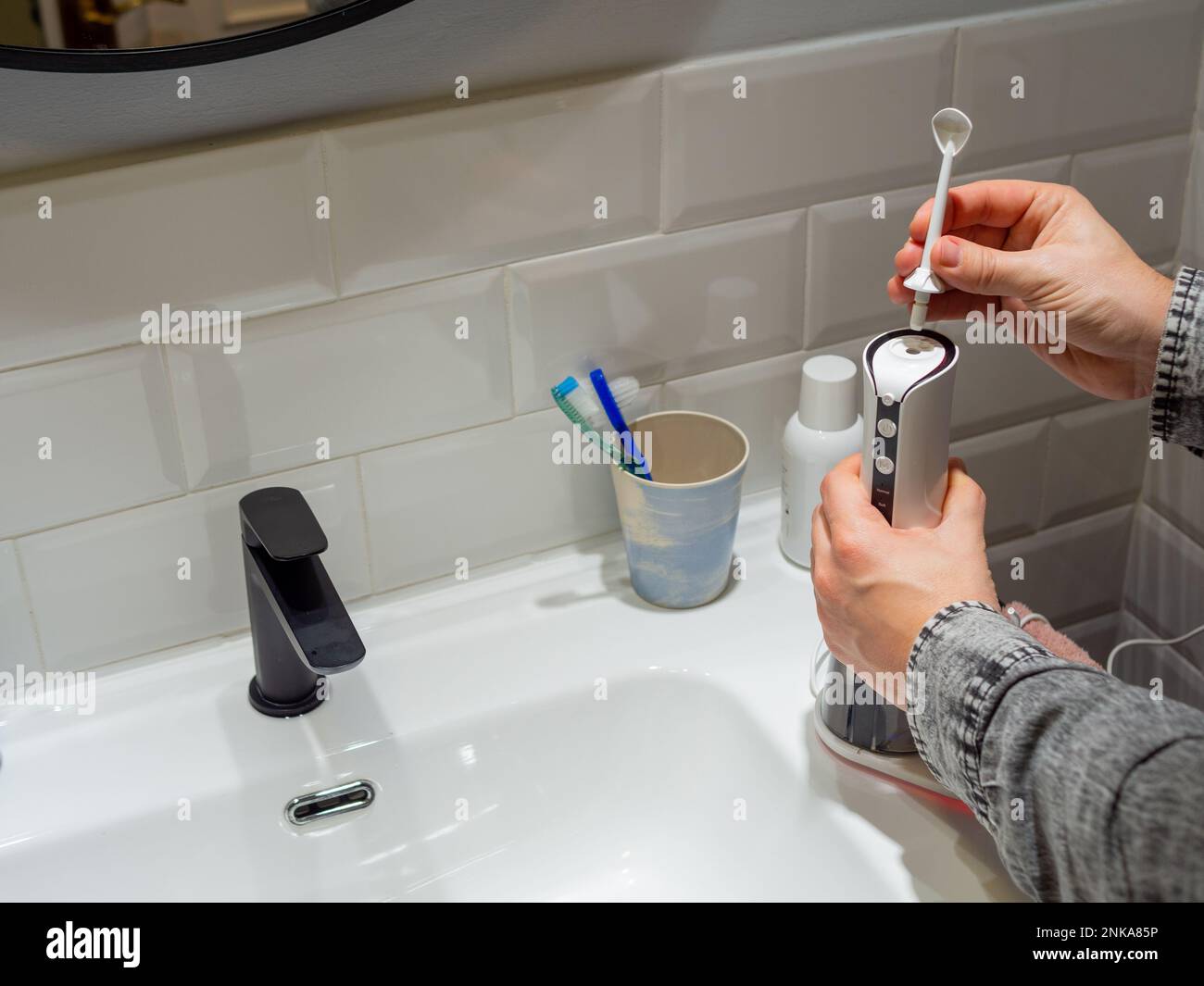 Le mani del giovane uomo che cambiano la sua punta domestica del flosser dell'acqua dentale Foto Stock