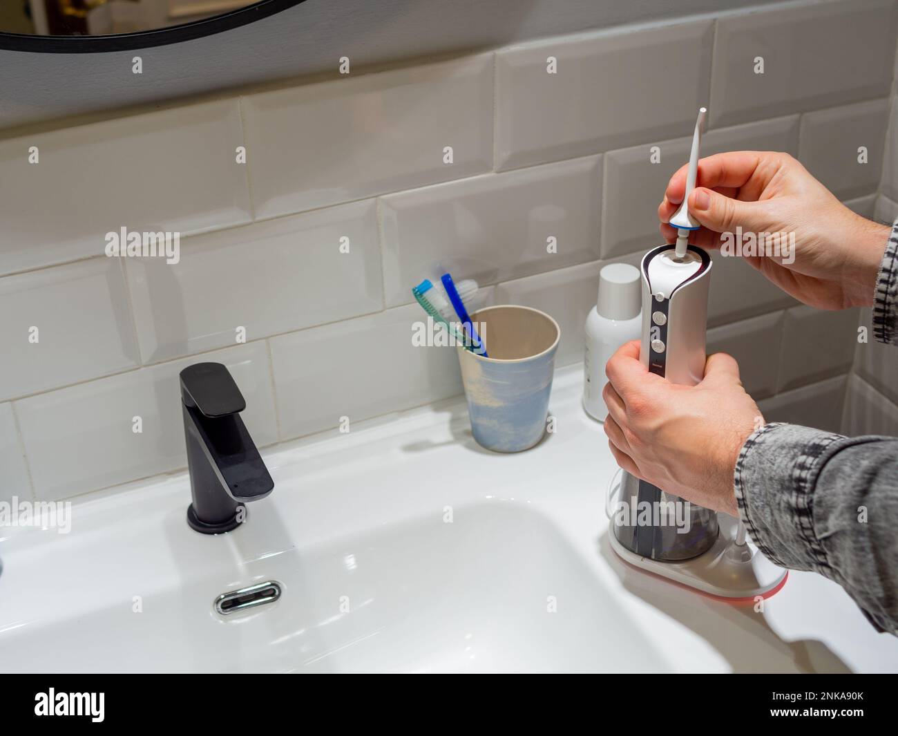 Le mani del giovane uomo che cambiano la sua punta domestica del flosser dell'acqua dentale Foto Stock