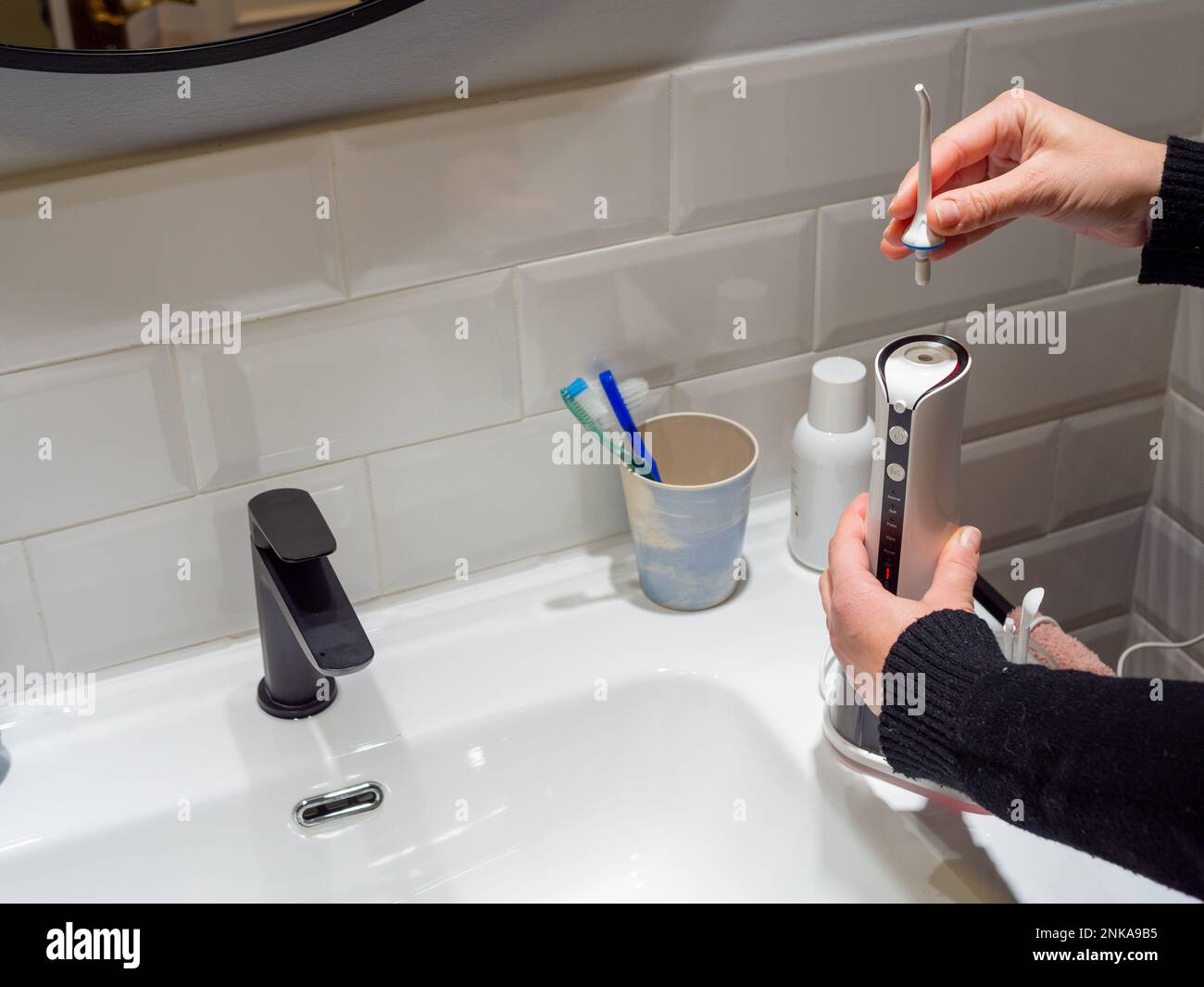 Le mani di giovane donna che cambiano la sua punta domestica del flosser dell'acqua dentale Foto Stock