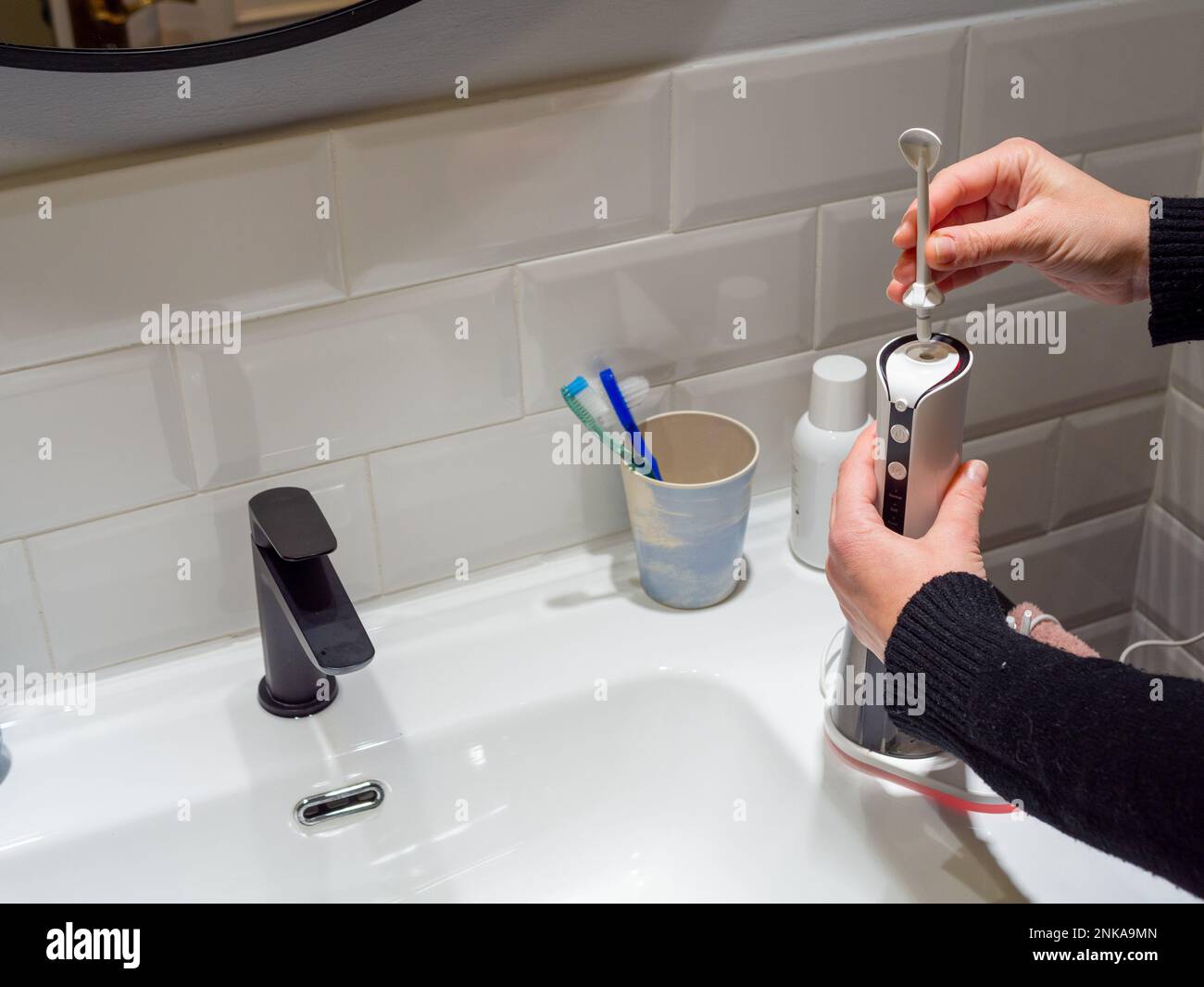 Le mani di giovane donna che cambiano la sua punta domestica del flosser dell'acqua dentale Foto Stock