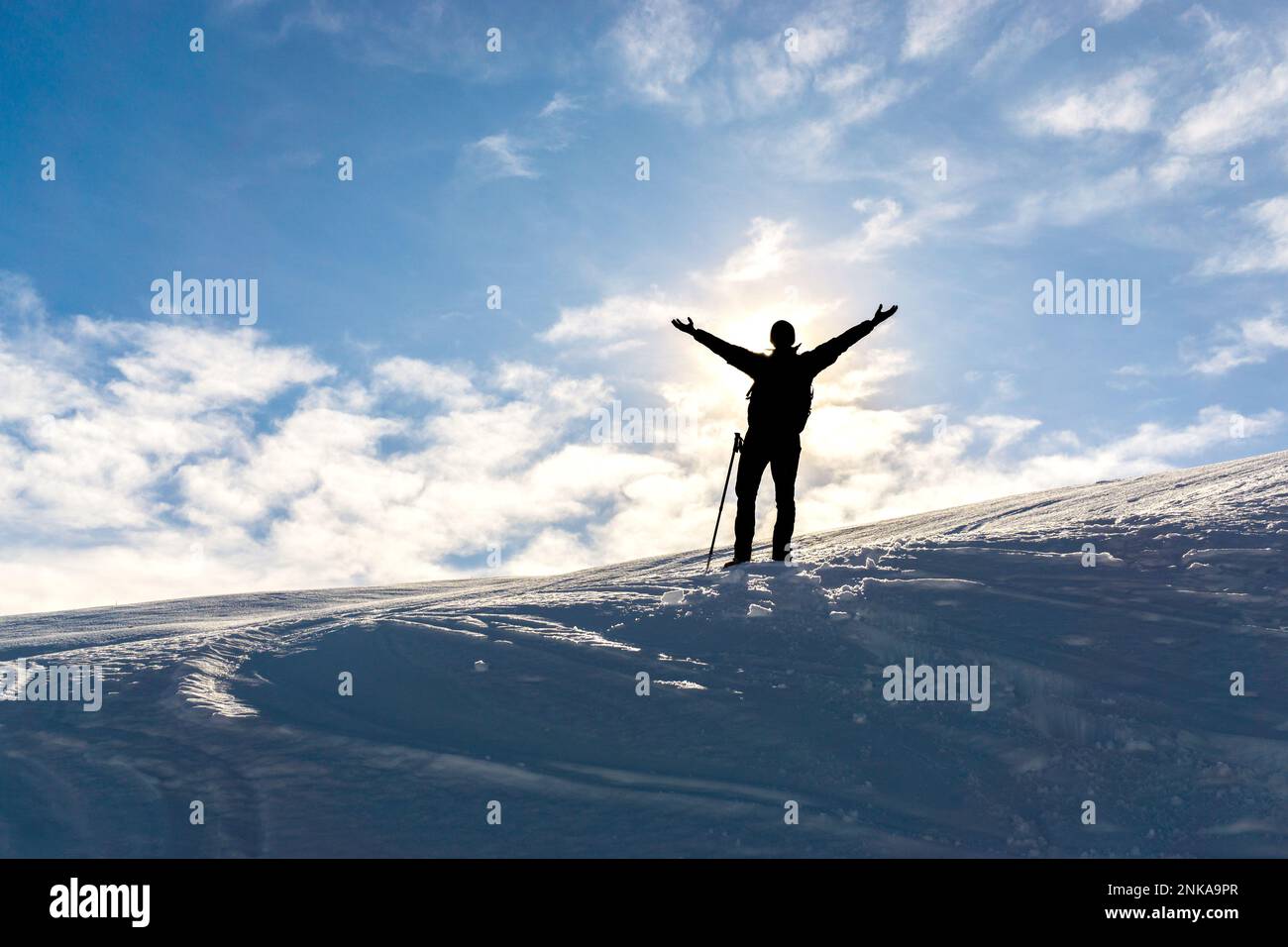 Silhouette di celebrare felice uomo escursionista con le braccia sollevate sulla neve montagna invernale. Sole dietro la persona. Foto Stock