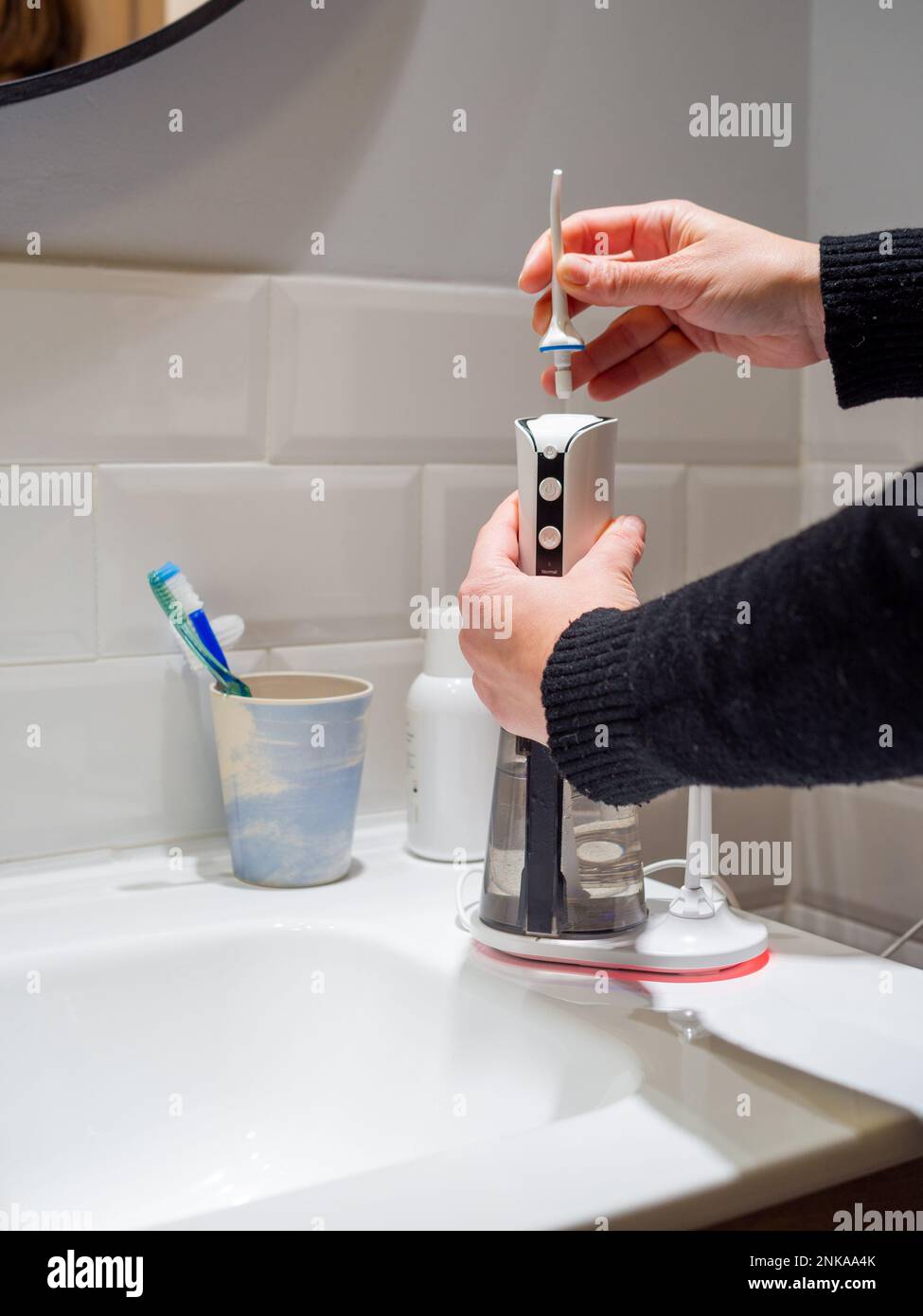 Le mani di giovane donna che cambiano la sua punta domestica del flosser dell'acqua dentale Foto Stock