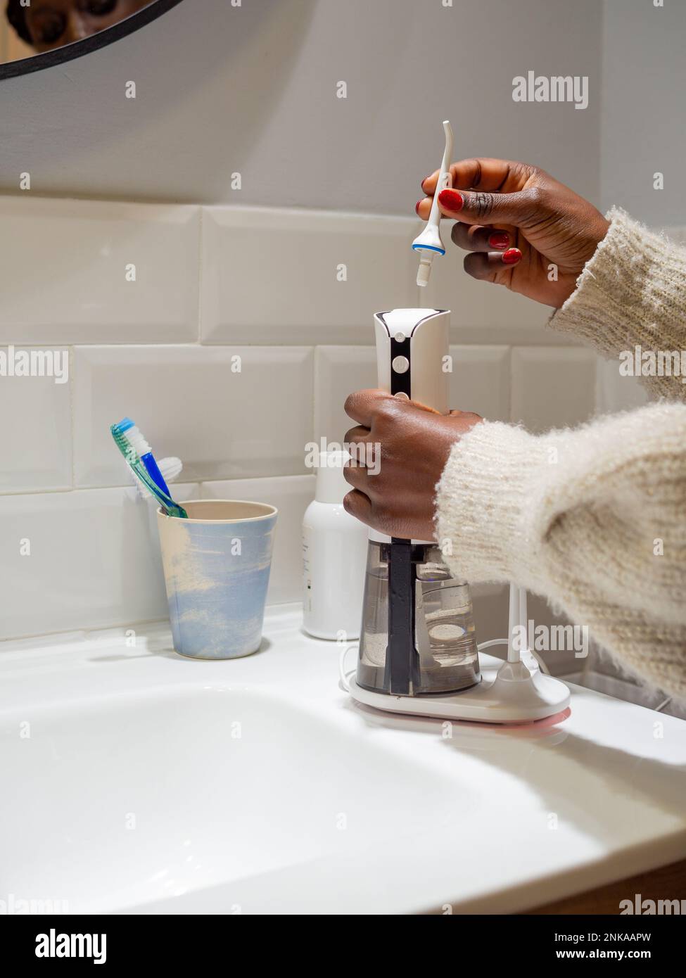 Le mani di giovane donna che cambiano la sua punta domestica del flosser dell'acqua dentale Foto Stock