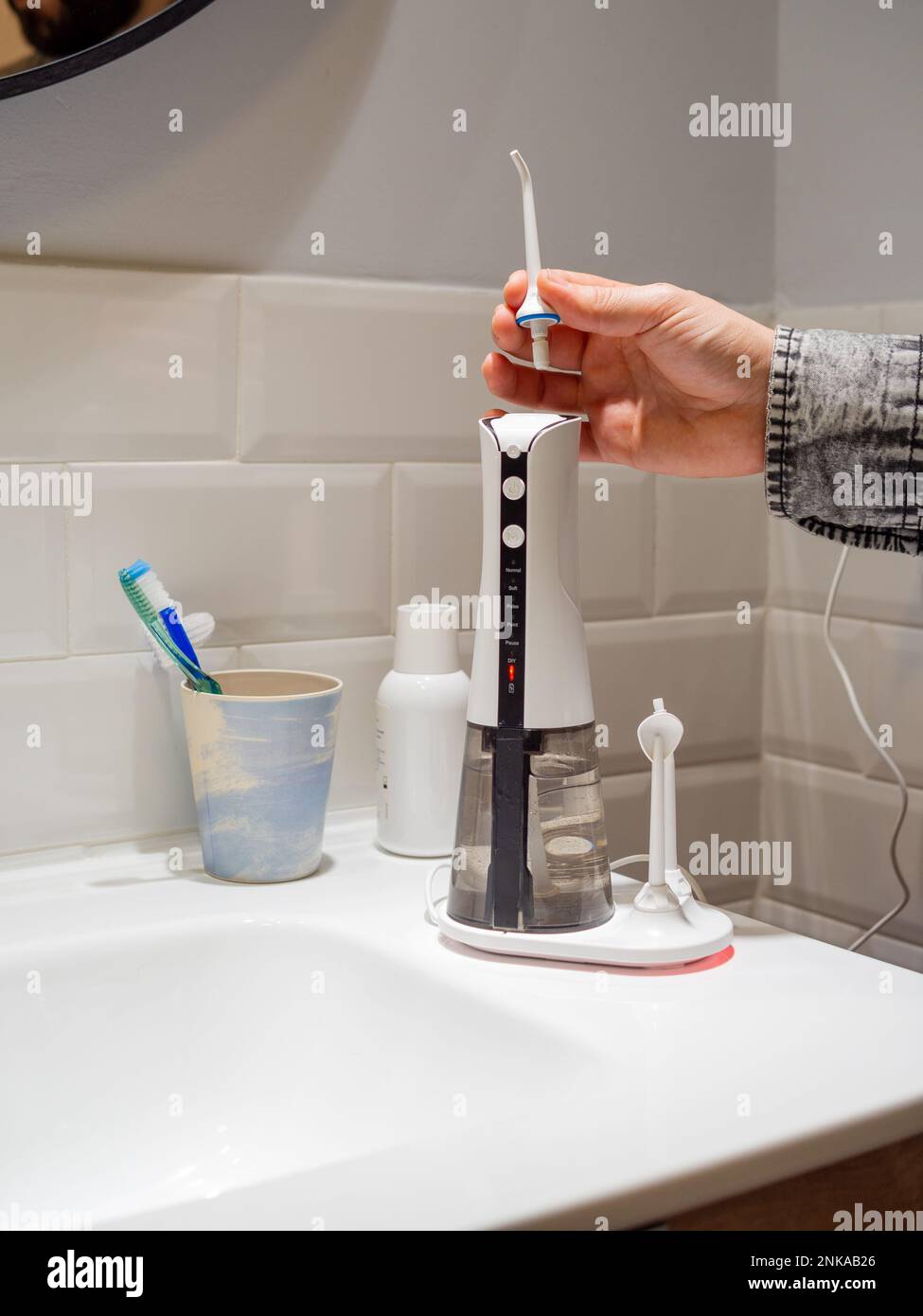 Le mani del giovane uomo che cambiano la sua punta domestica del flosser dell'acqua dentale Foto Stock