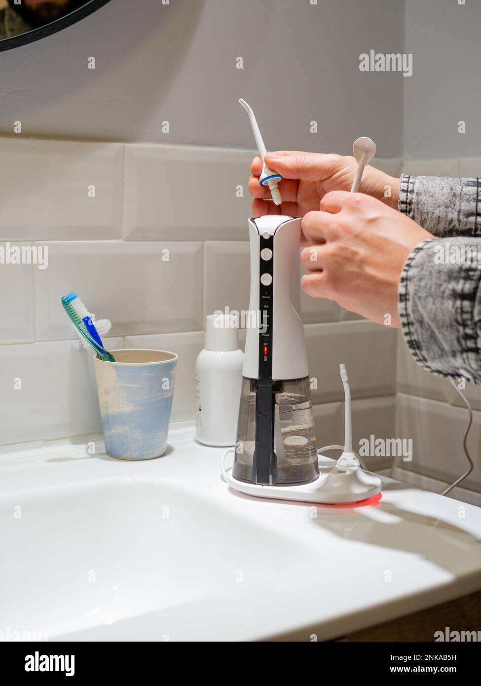 Le mani del giovane uomo che cambiano la sua punta domestica del flosser dell'acqua dentale Foto Stock