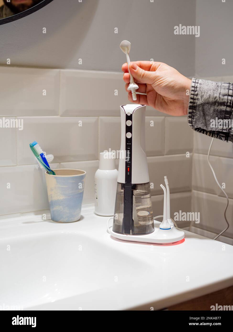 Le mani del giovane uomo che cambiano la sua punta domestica del flosser dell'acqua dentale Foto Stock