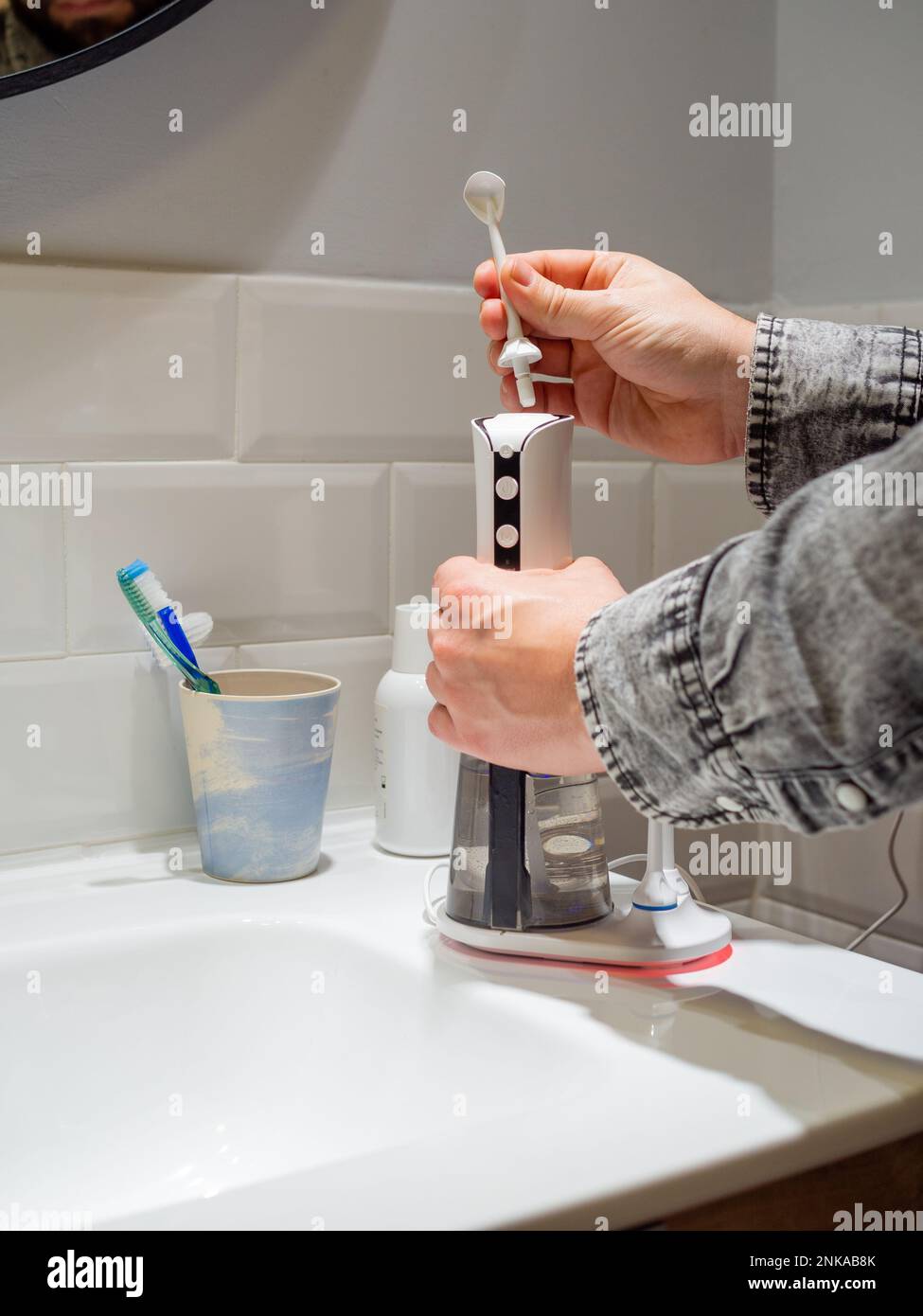 Le mani del giovane uomo che cambiano la sua punta domestica del flosser dell'acqua dentale Foto Stock