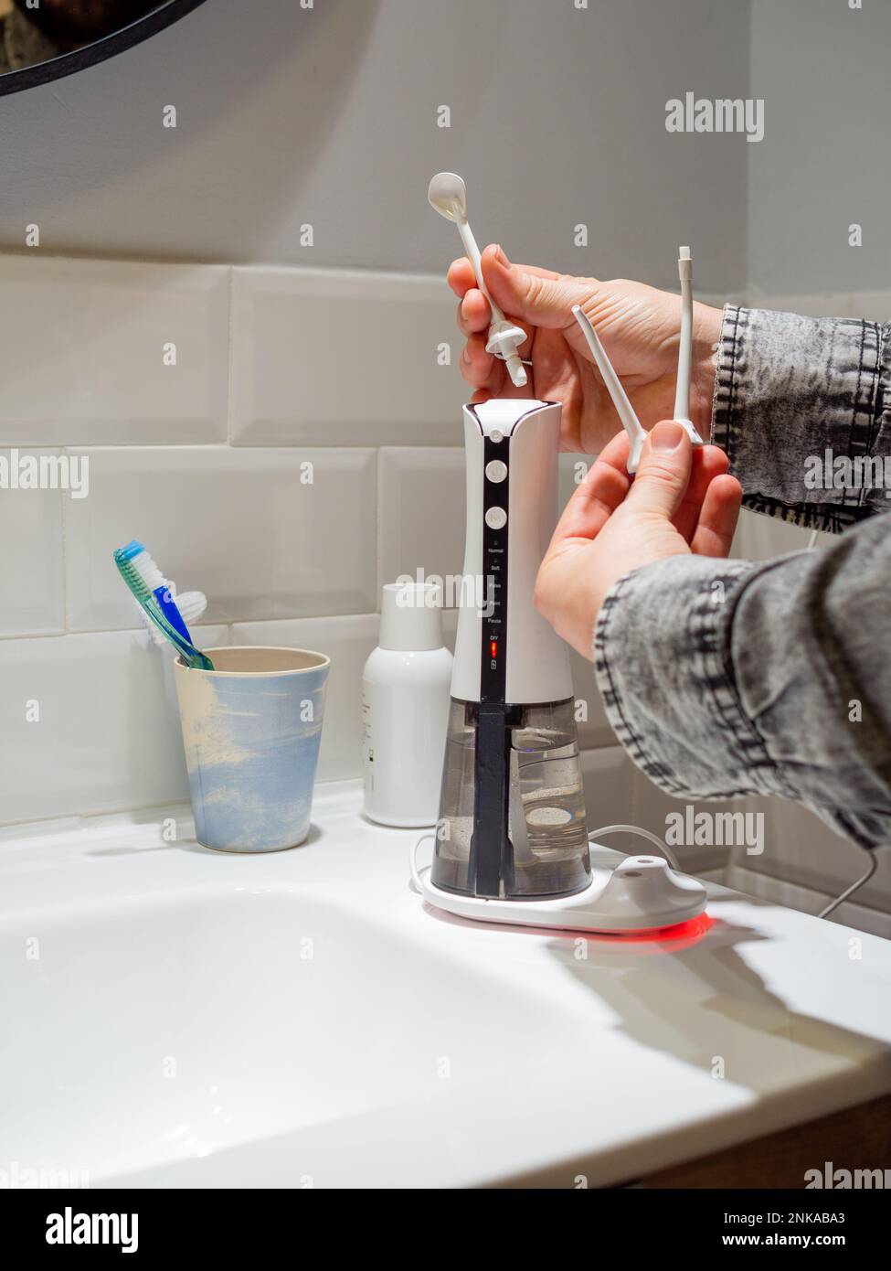 Le mani del giovane uomo che cambiano la sua punta domestica del flosser dell'acqua dentale Foto Stock