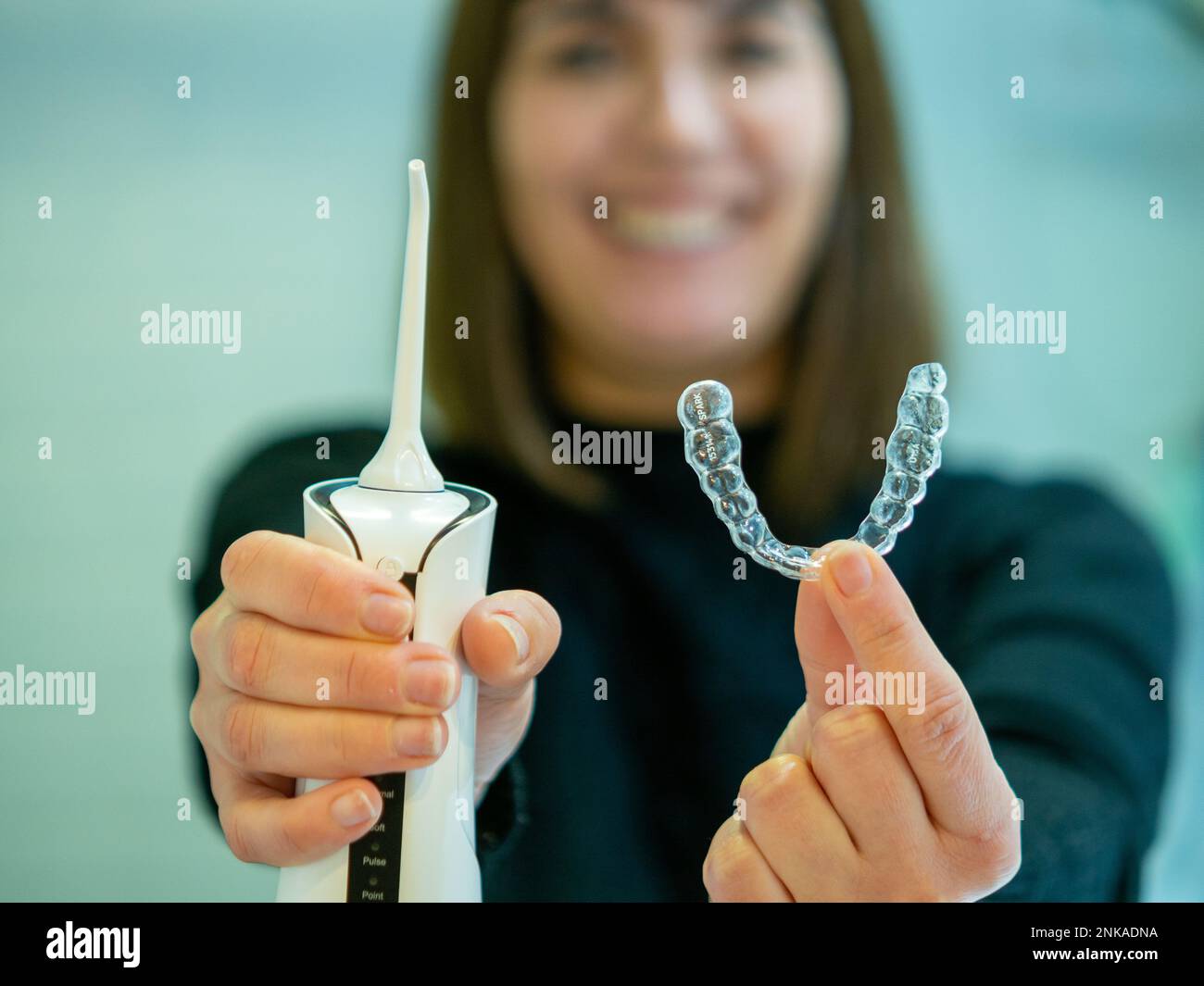 Mantenere un sorriso sano: Una giovane donna esegue la sua routine di igiene dentale a casa utilizzando un flosser d'acqua dentale domestico e il suo allineatore dentale. Foto Stock