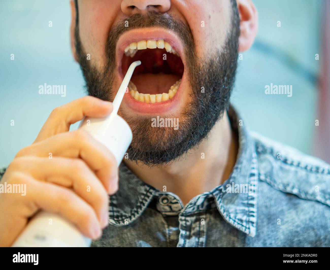 Igiene orale sana: Giovane uomo che usa il flosser domestico dell'acqua dentale Foto Stock