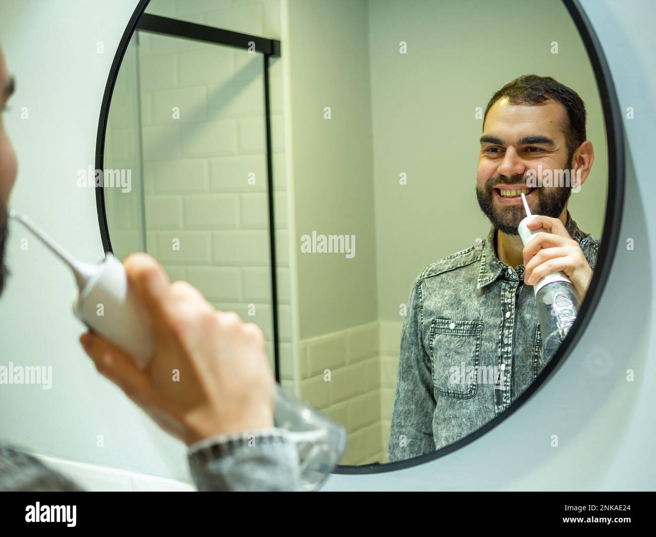 Igiene orale sana: Giovane uomo che usa il flosser domestico dell'acqua dentale nello specchio del bagno Foto Stock