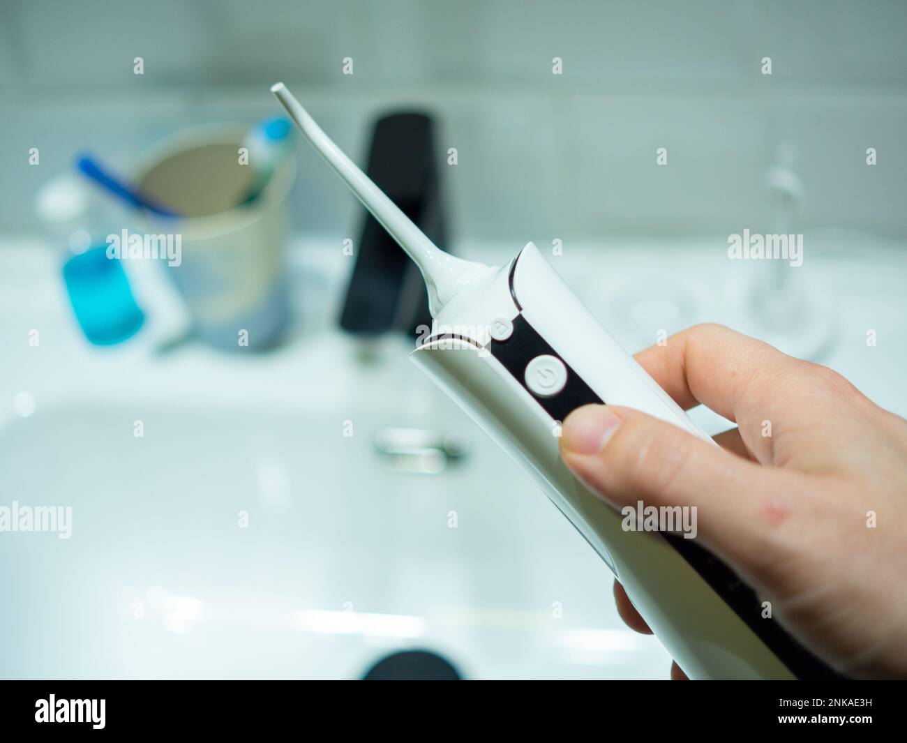 mano di un giovane uomo che tiene un galleggiante d'acqua domestico dentale davanti ad un lavabo del bagno Foto Stock