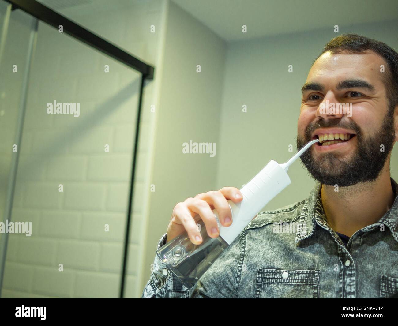 Igiene orale sana: Giovane uomo che usa il flosser domestico dell'acqua dentale nello specchio del bagno Foto Stock