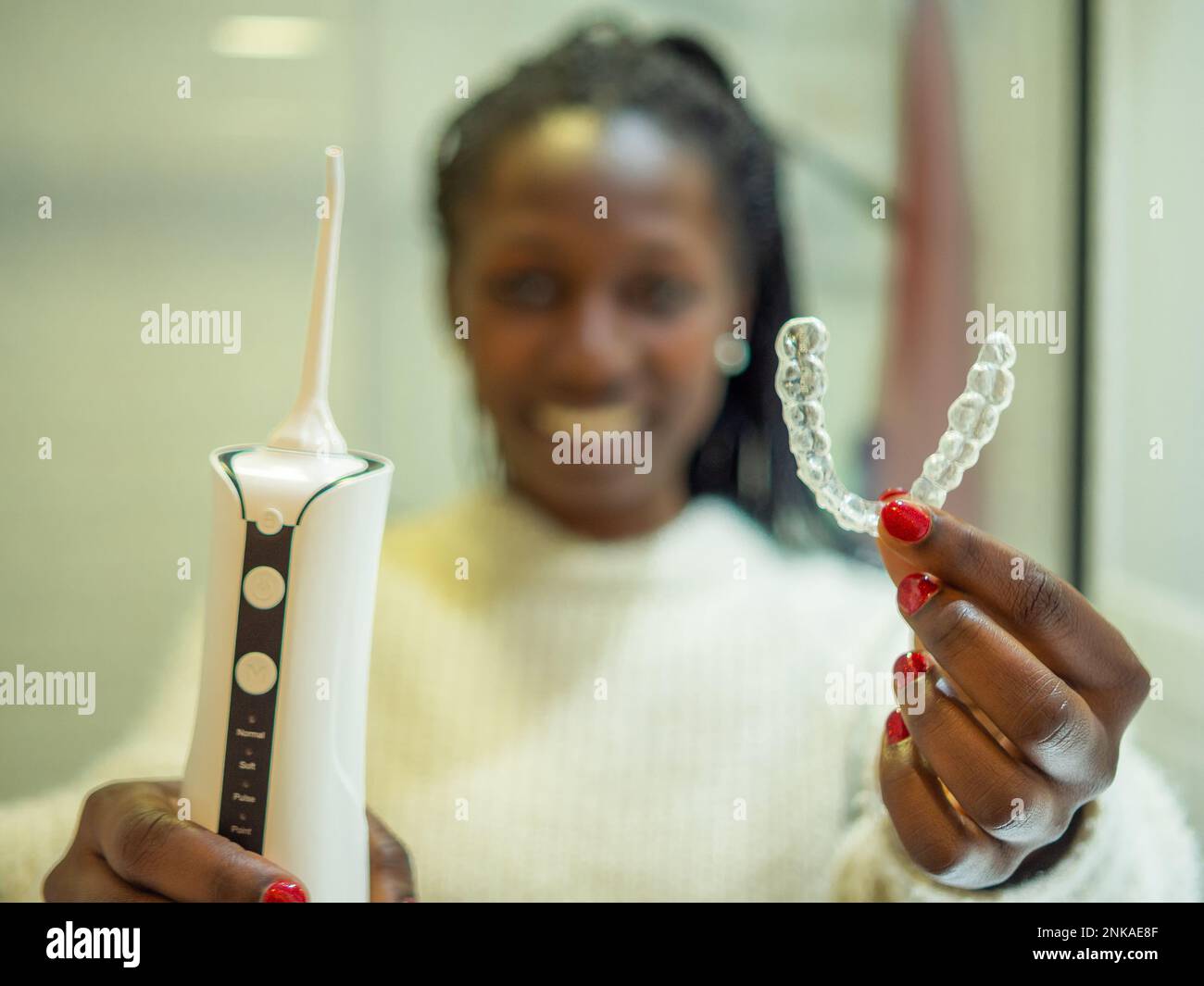Mantenere un sorriso sano: Una giovane donna esegue la sua routine di igiene dentale a casa utilizzando un flosser d'acqua dentale domestico e il suo allineatore dentale. Foto Stock