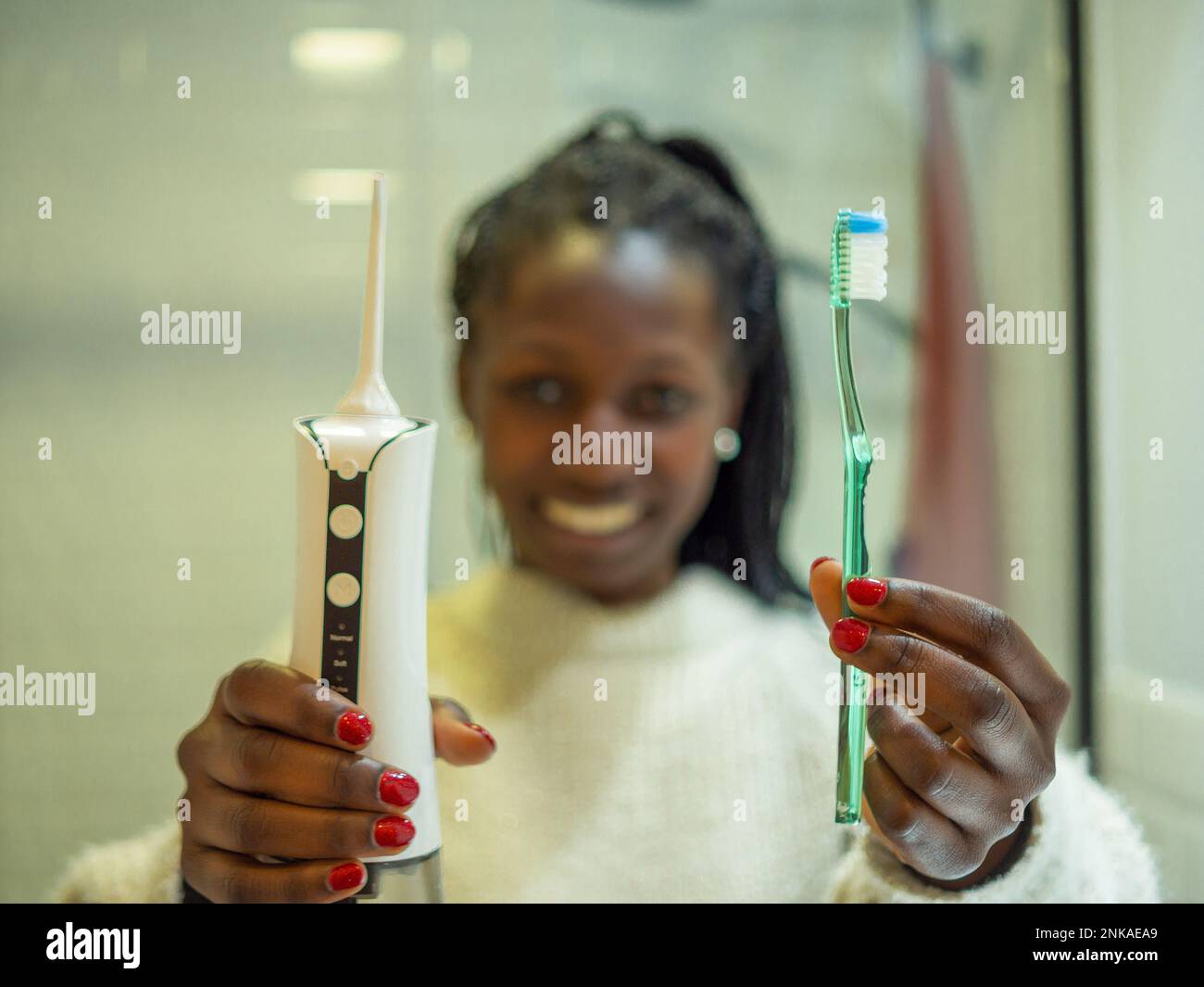 Mantenere un sorriso sano: Una giovane donna esegue la sua routine di igiene dentale a casa utilizzando un flosser d'acqua dentale domestico e il suo dentifro dentale Foto Stock
