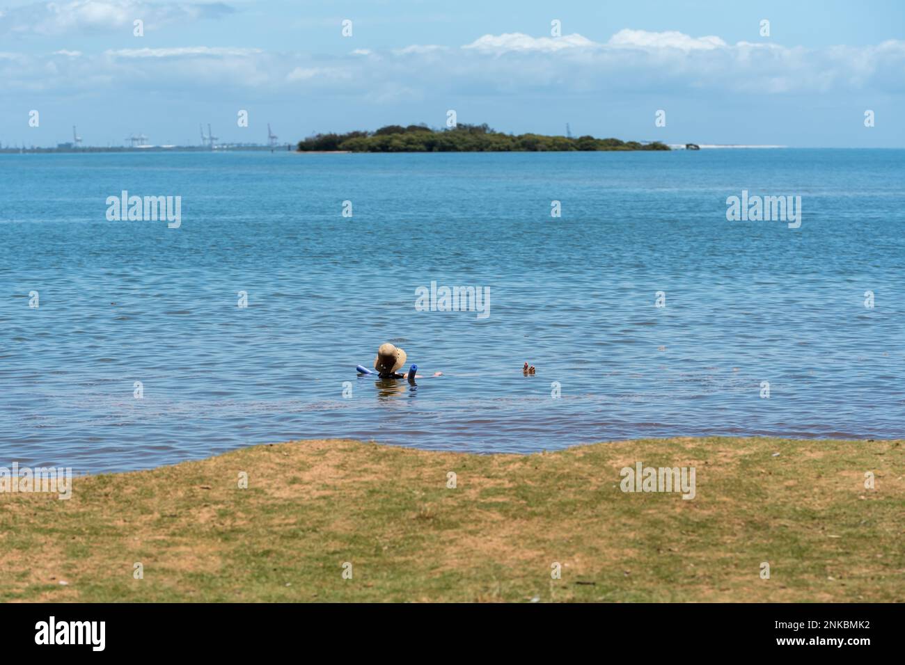 Scena della spiaggia con una persona che galleggia in acqua mentre guarda fuori attraverso la baia fino a King Island in lontananza. Foto Stock