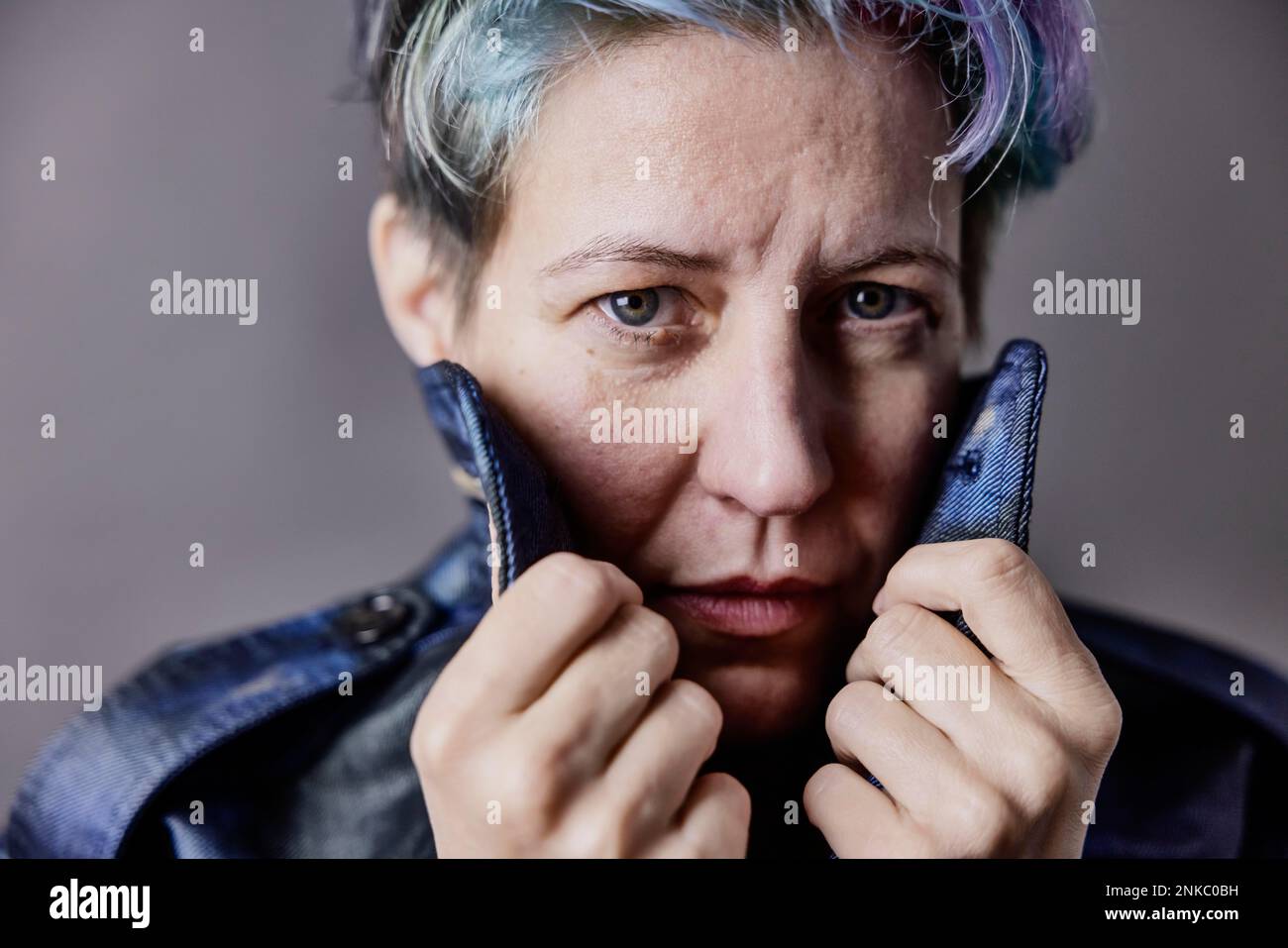 Donna androgina con i capelli tinti tira il colletto della sua giacca in denim, ritratto Foto Stock