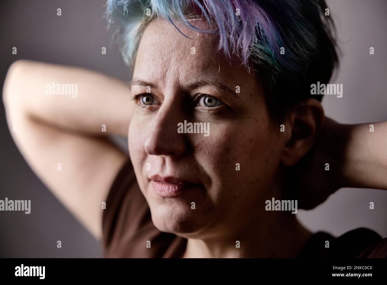 Donna androgina con i capelli tinti attraversa le braccia dietro la testa, ritratto Foto Stock