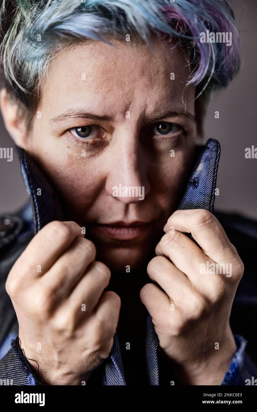 Donna androgina con i capelli tinti tira il colletto della sua giacca in denim, ritratto Foto Stock