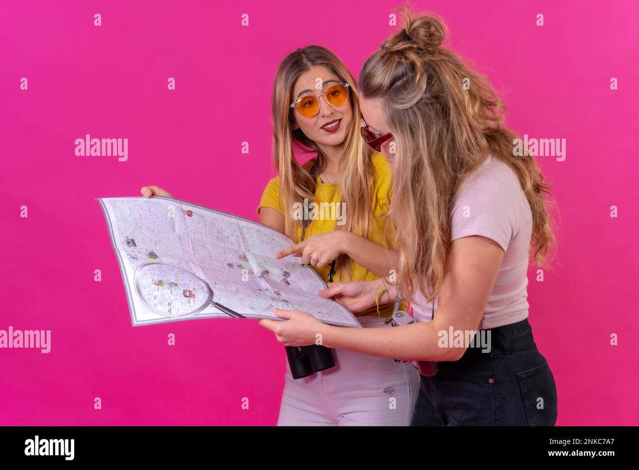 Due giovani donne caucasiche bionde che guardano una mappa della città, isolate su uno sfondo rosa Foto Stock