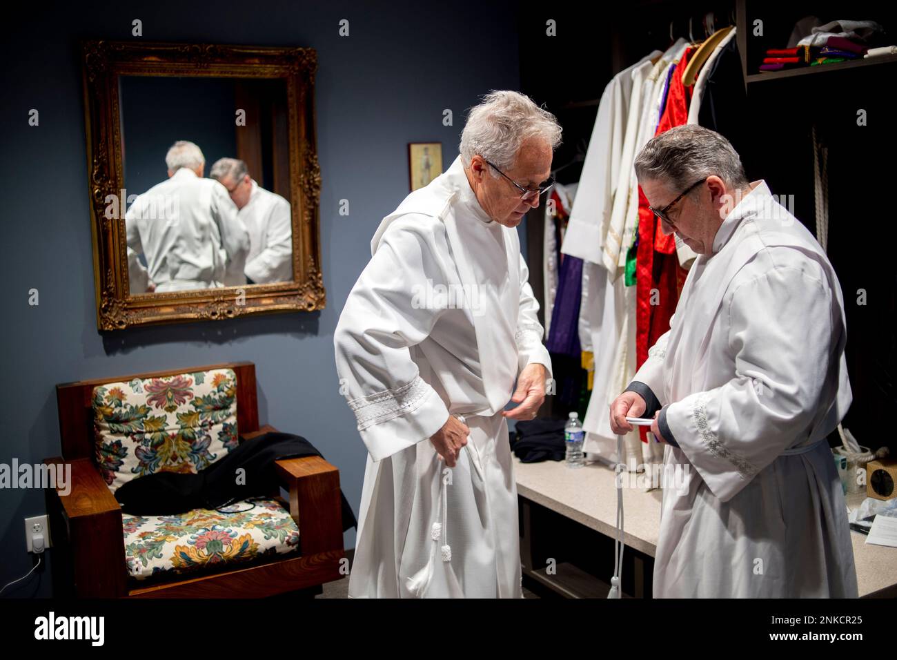 Deacon Dennis Pennell, left, and Deacon Dan Medich Jr. each get their formal robes on before joining Father Joe Krupp, pastor at Church of the Holy Family, as each spreads Good Friday faith and prayer through Grand Blanc, Mich., neighborhood on Friday, April 15, 2022. (Jake May/The Flint Journal via AP) Foto Stock
