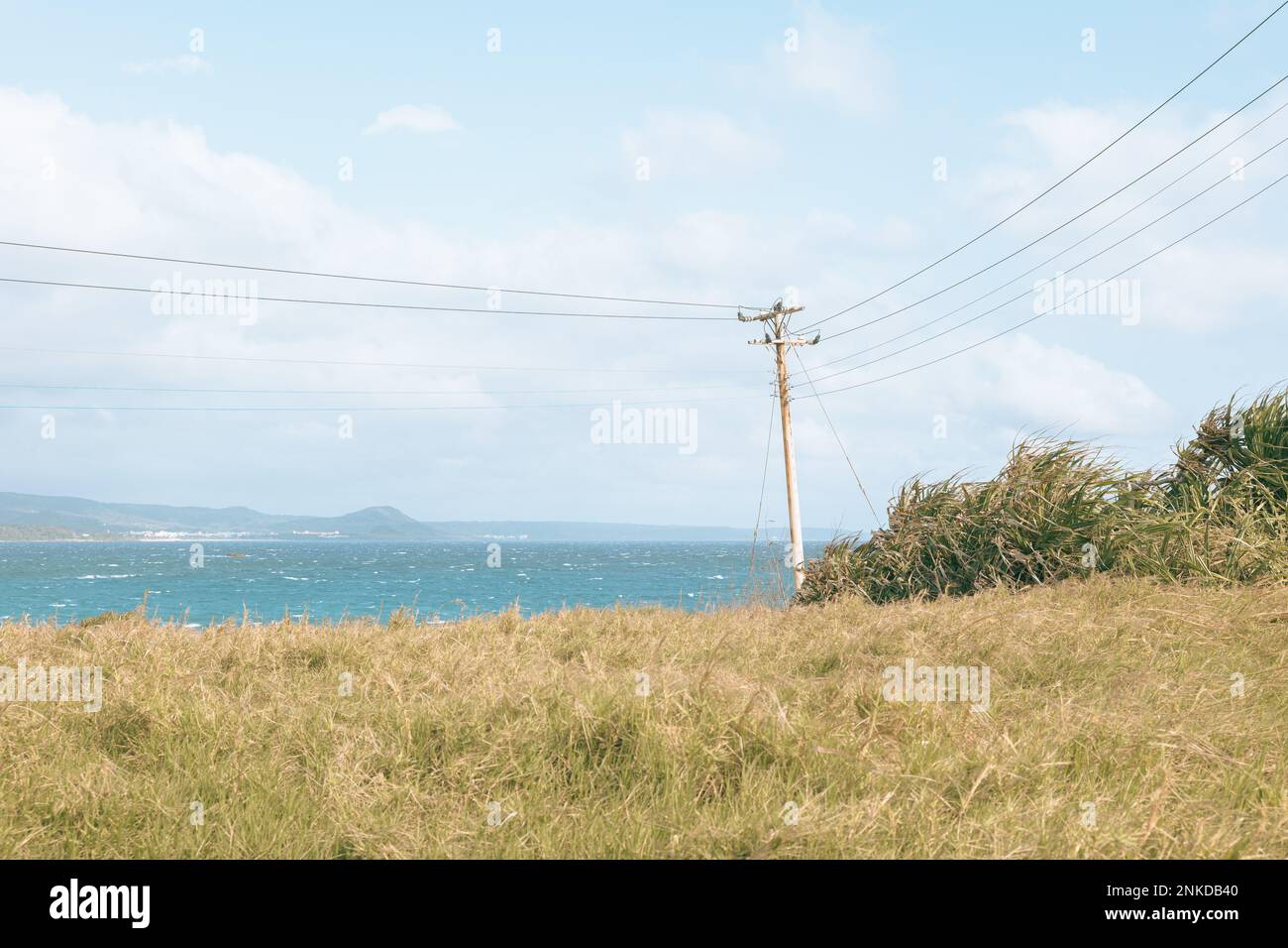 Vecchio palo telefonico in piedi sul mare con oceano e montaisn sullo sfondo e una collina di erba in primo piano Foto Stock