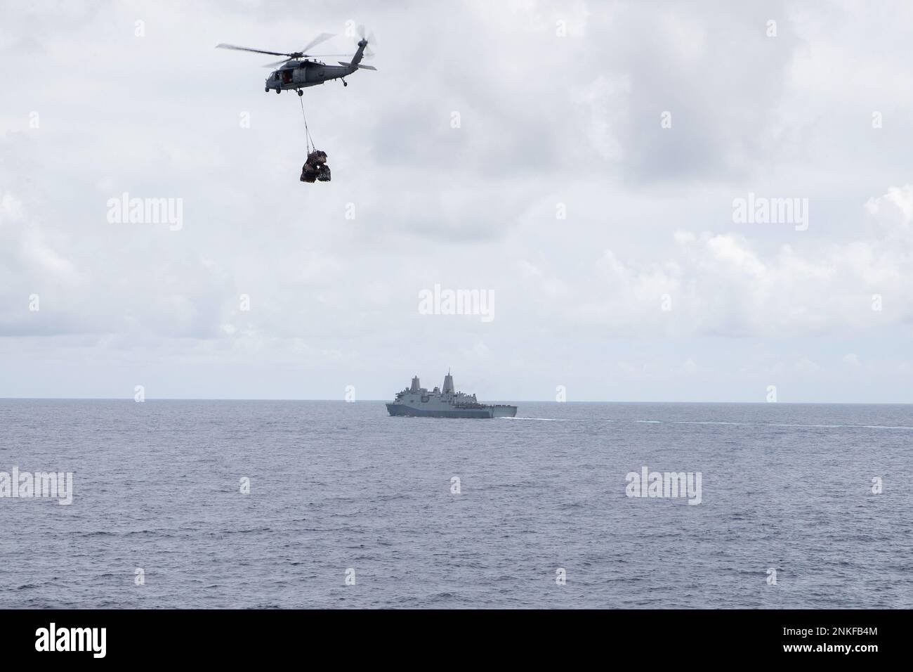 220815-N-XN177-1121 MARE DELLE FILIPPINE (15 agosto 2022) – un elicottero MH-60s Sea Hawk assegnato a Helicopter Sea Combat Squadron (HSC) 23 vola un pallet di rifornimenti al vettore d'assalto anfibio USS Tripoli (LHA 7), mentre il molo di trasporto anfibio USS New Orleans (LPD 18) batte nelle vicinanze durante un rifornimento verticale, 15 agosto 2022. Tripoli opera nell'area delle operazioni della flotta 7th degli Stati Uniti per migliorare l'interoperabilità con alleati e partner e fungere da pronta forza di risposta per difendere la pace e mantenere la stabilità nella regione dell'Indo-Pacifico. Foto Stock
