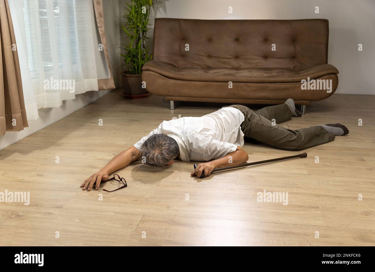 Uomo anziano asiatico che cade e si trova sul pavimento mentre cammina con bastone a piedi a casa. Foto Stock