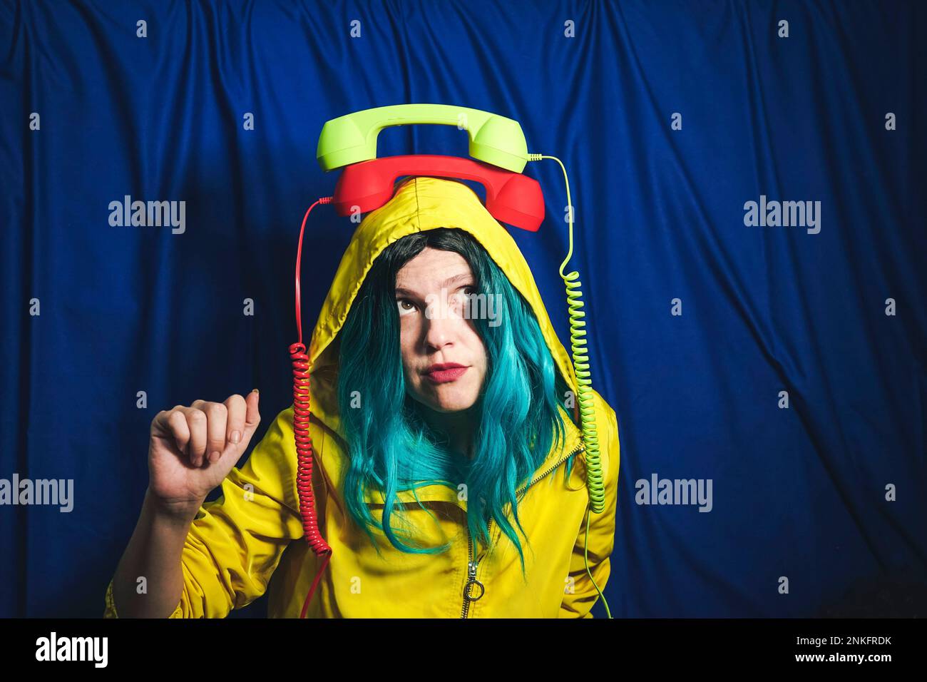 Donna che bilancia i ricevitori telefonici verdi e rossi sulla testa di fronte allo sfondo blu Foto Stock