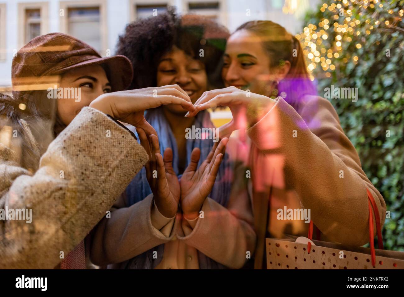 Amici felici che formano il cuore insieme alle mani che si vedono attraverso il vetro Foto Stock