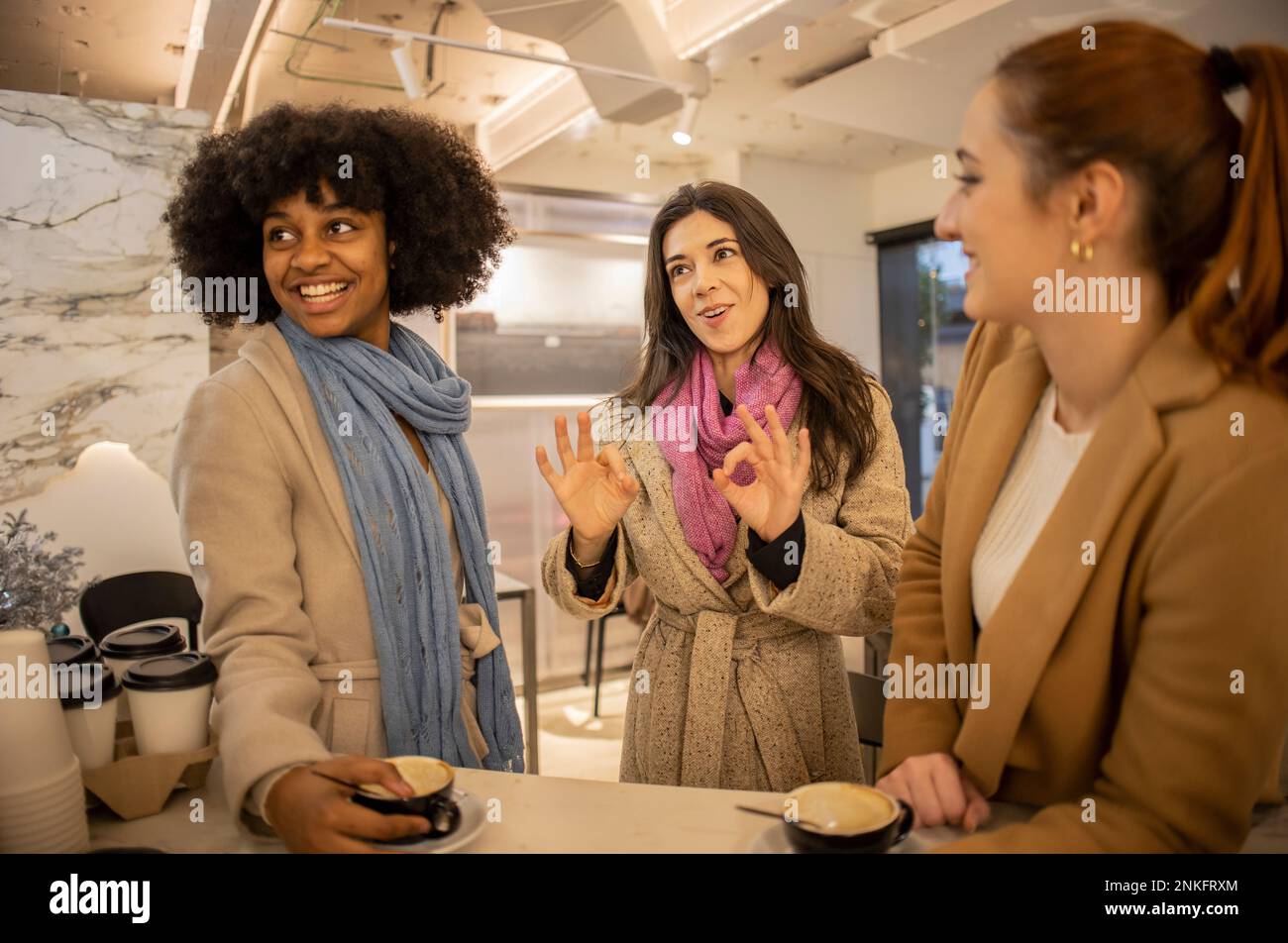 Donna felice che mostra un gesto OK con gli amici in piedi al tavolo Foto Stock