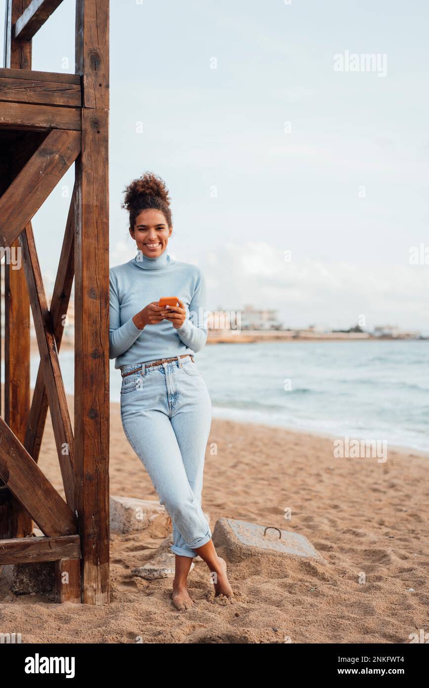 Giovane donna sorridente appoggiata su una struttura in legno Foto Stock