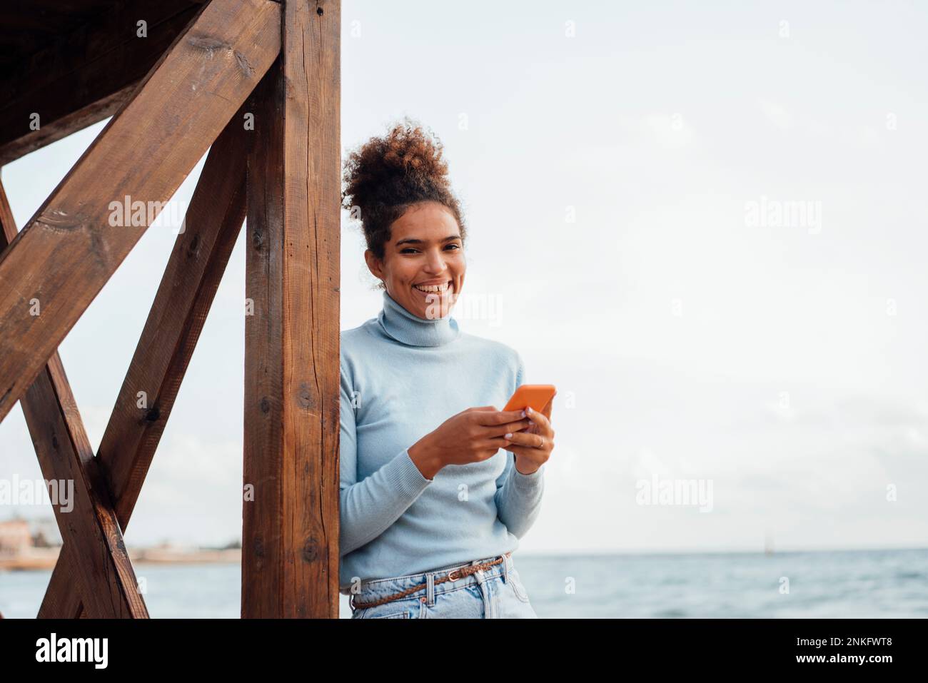 Donna felice con telefono cellulare in piedi da struttura in legno Foto Stock