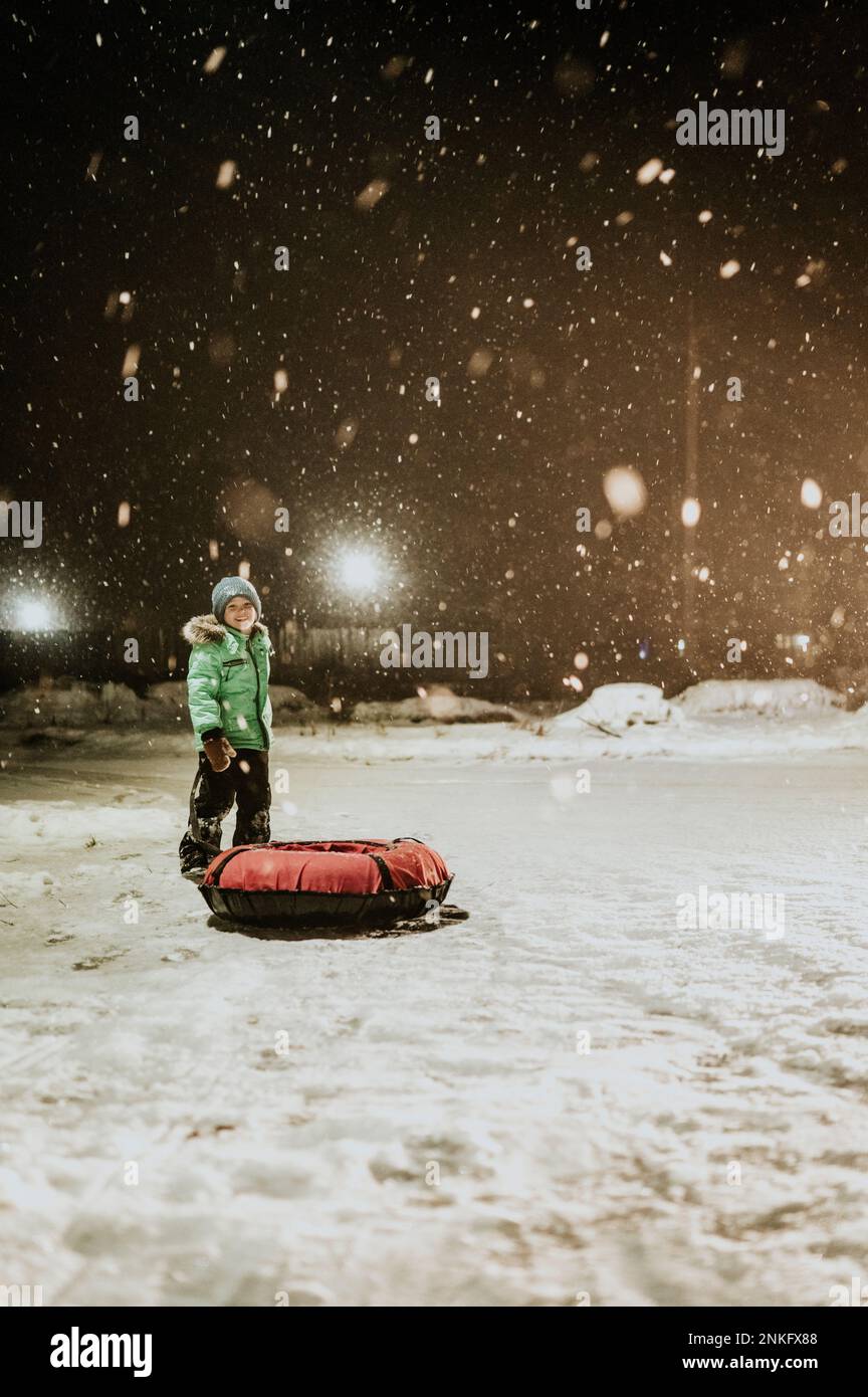 Ragazzo con slitta gonfiabile in piedi nella neve di notte Foto Stock
