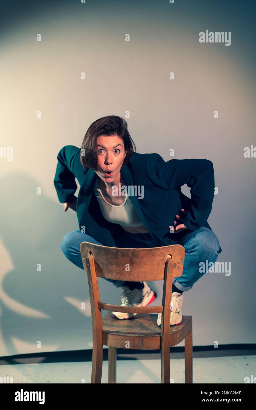 Donna d'affari che fa i volti seduti davanti allo sfondo Foto Stock