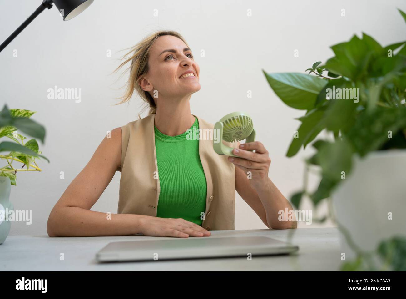 Felice freelancer con il ventilatore motorizzato portatile seduto alla scrivania Foto Stock