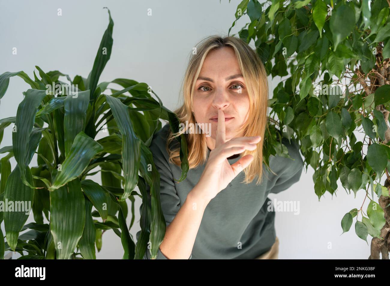 Donna in piedi con il dito sulle labbra in mezzo alle piante Foto Stock
