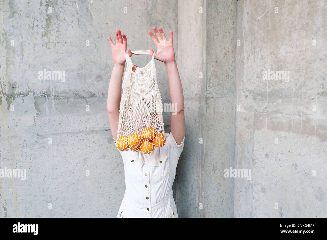Persona non binaria con borsa di arance davanti al muro Foto Stock