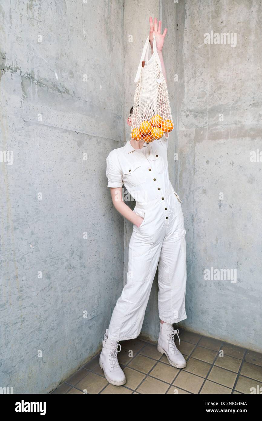 Persona non binaria che tiene la borsa di arance in piedi davanti al muro Foto Stock
